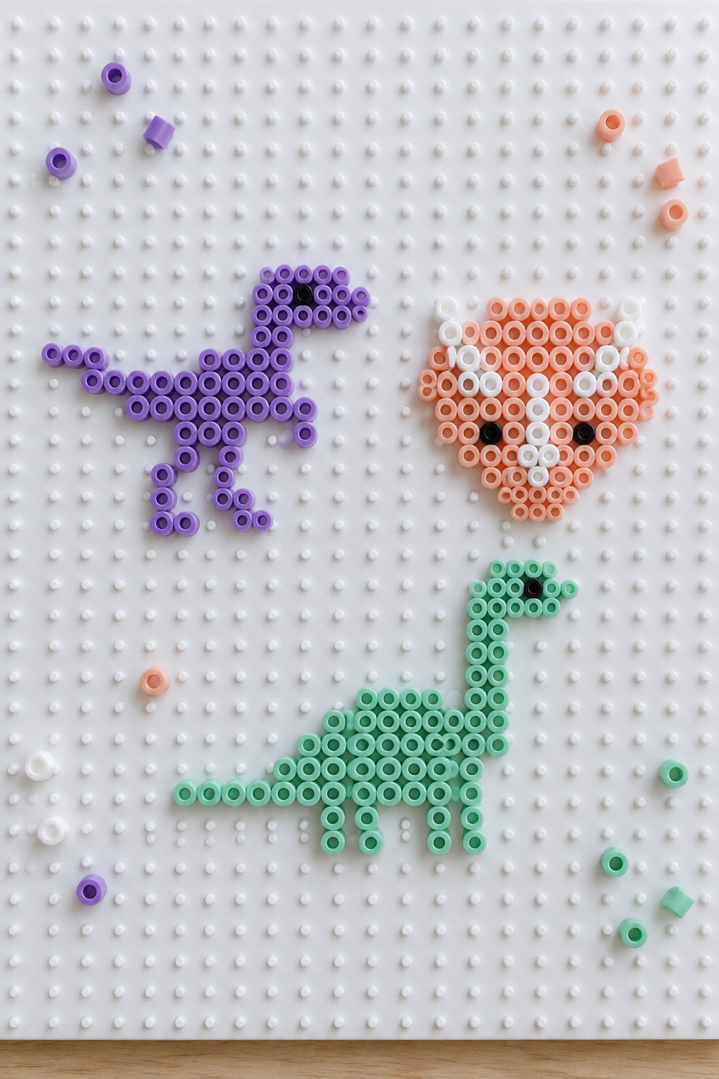 Purple dinosaur, green sauropod, and orange-white face made of Perler beads on pegboard.