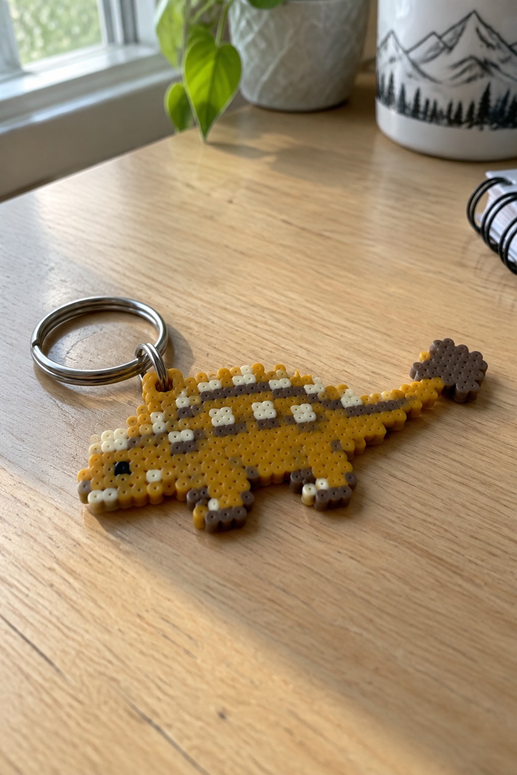 Yellow perler bead dinosaur keychain with metal ring on wooden table