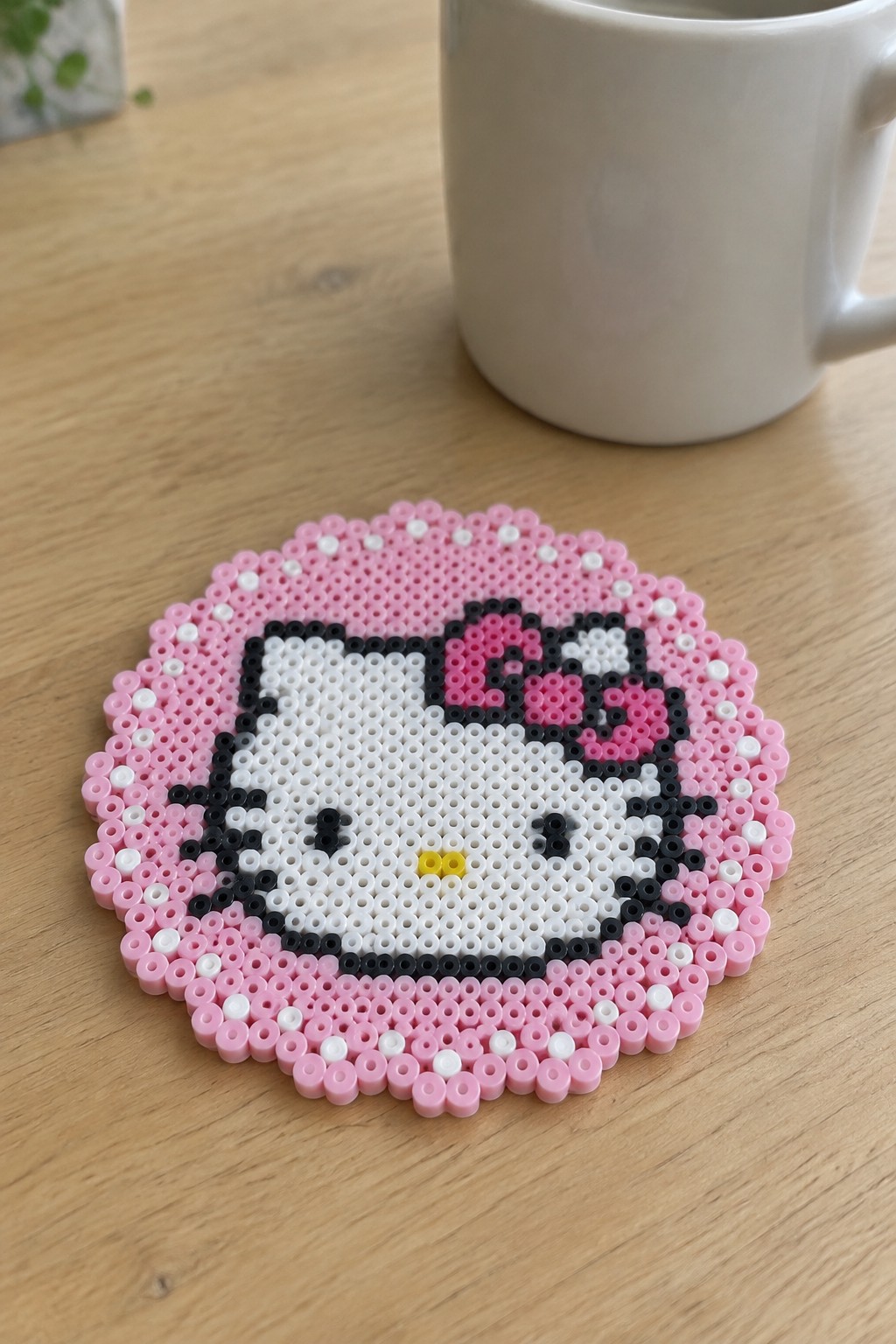 Hello Kitty perler bead coaster on wooden table beside white mug