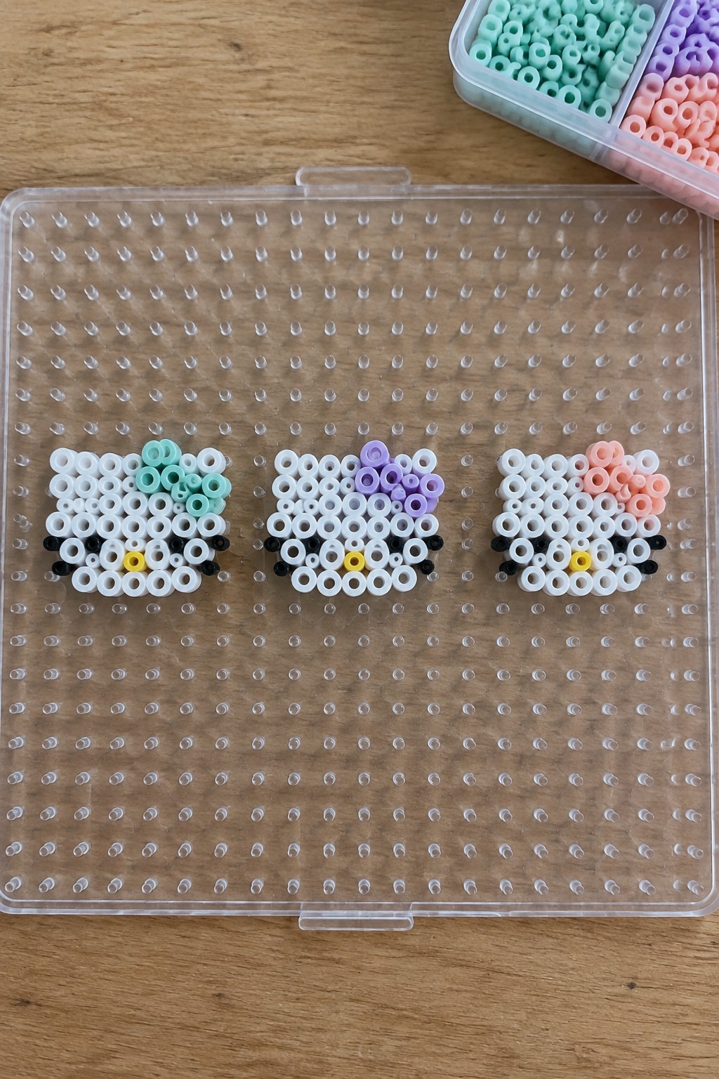Three Hello Kitty perler bead figures with pastel bows on a pegboard.
