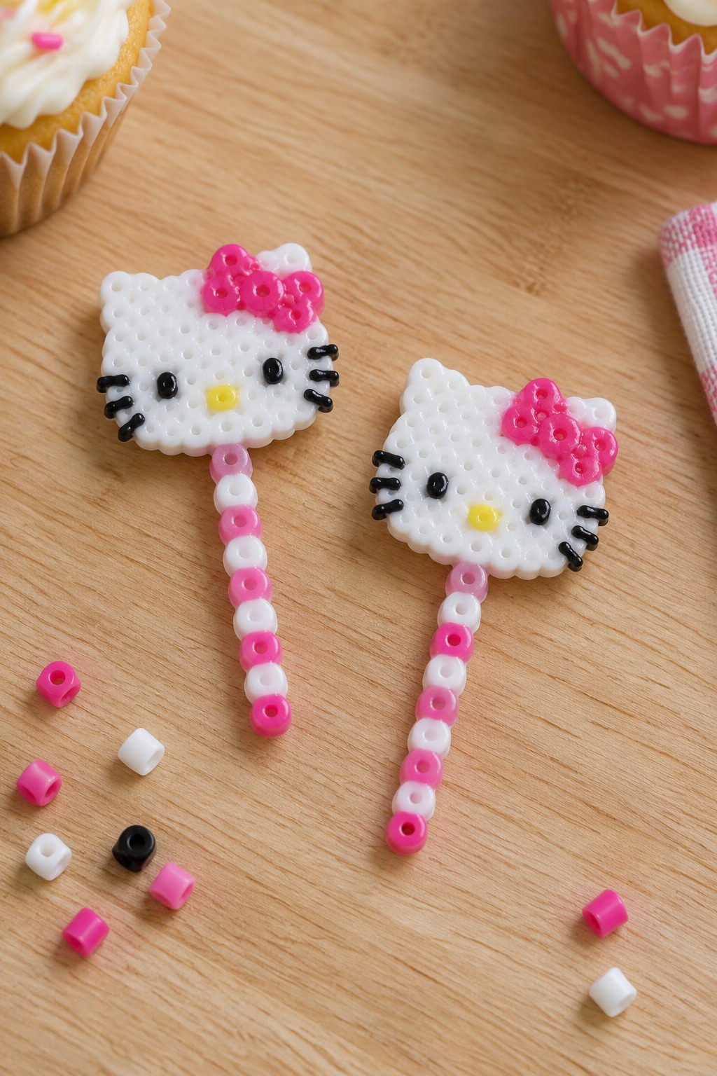 Two Hello Kitty perler bead figures with pink bows on wooden table
