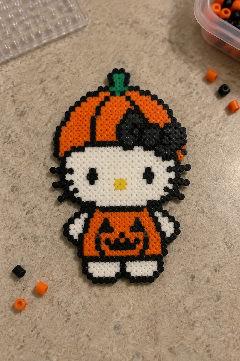 Hello Kitty perler bead figure in orange pumpkin Halloween costume on countertop