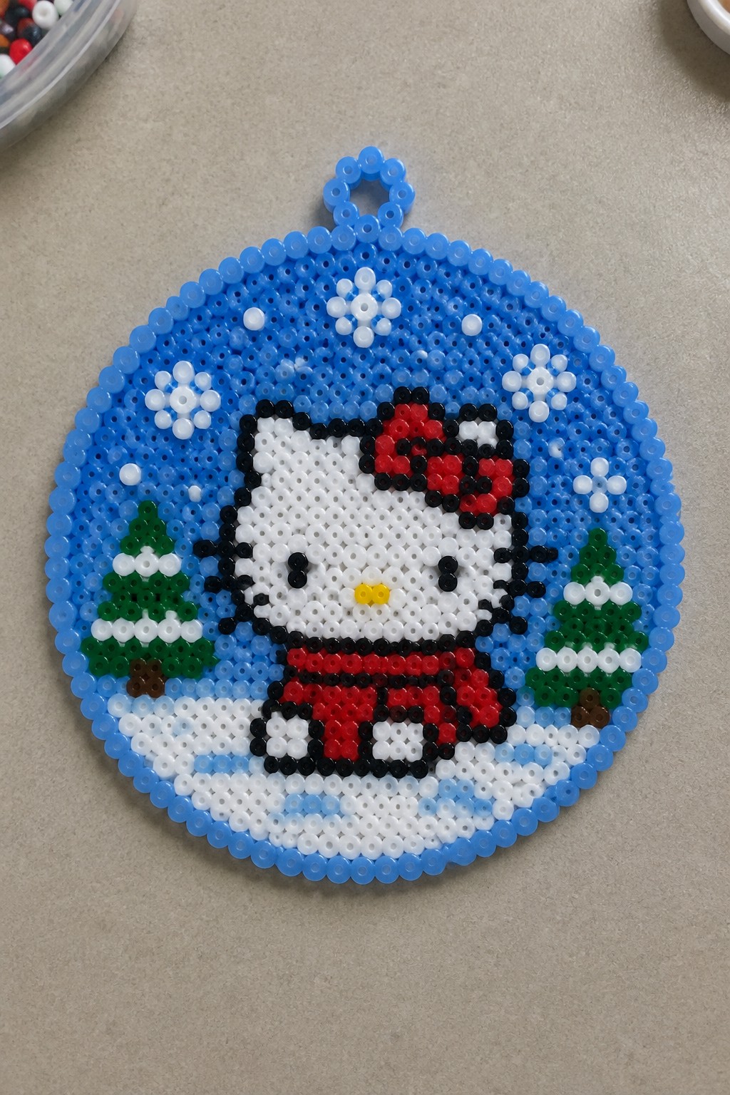 Beaded Hello Kitty Christmas ornament with snowy trees and snowflakes.