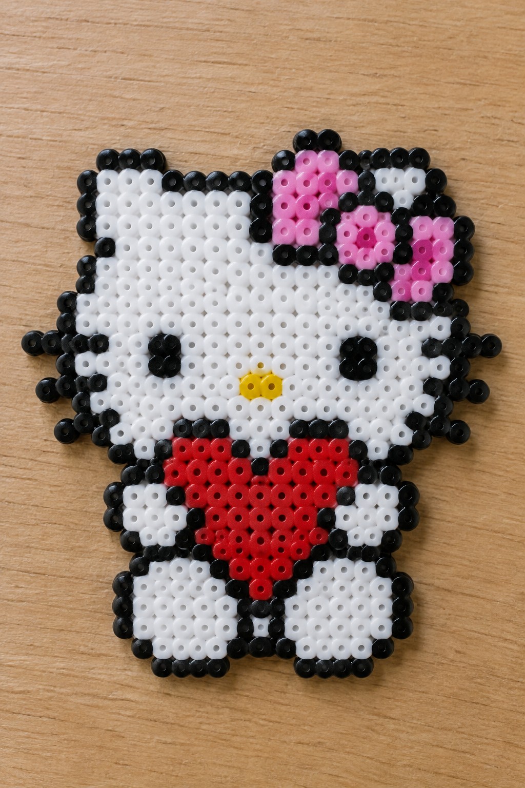 Perler bead Hello Kitty with pink bow, black ears, red collar on wood.