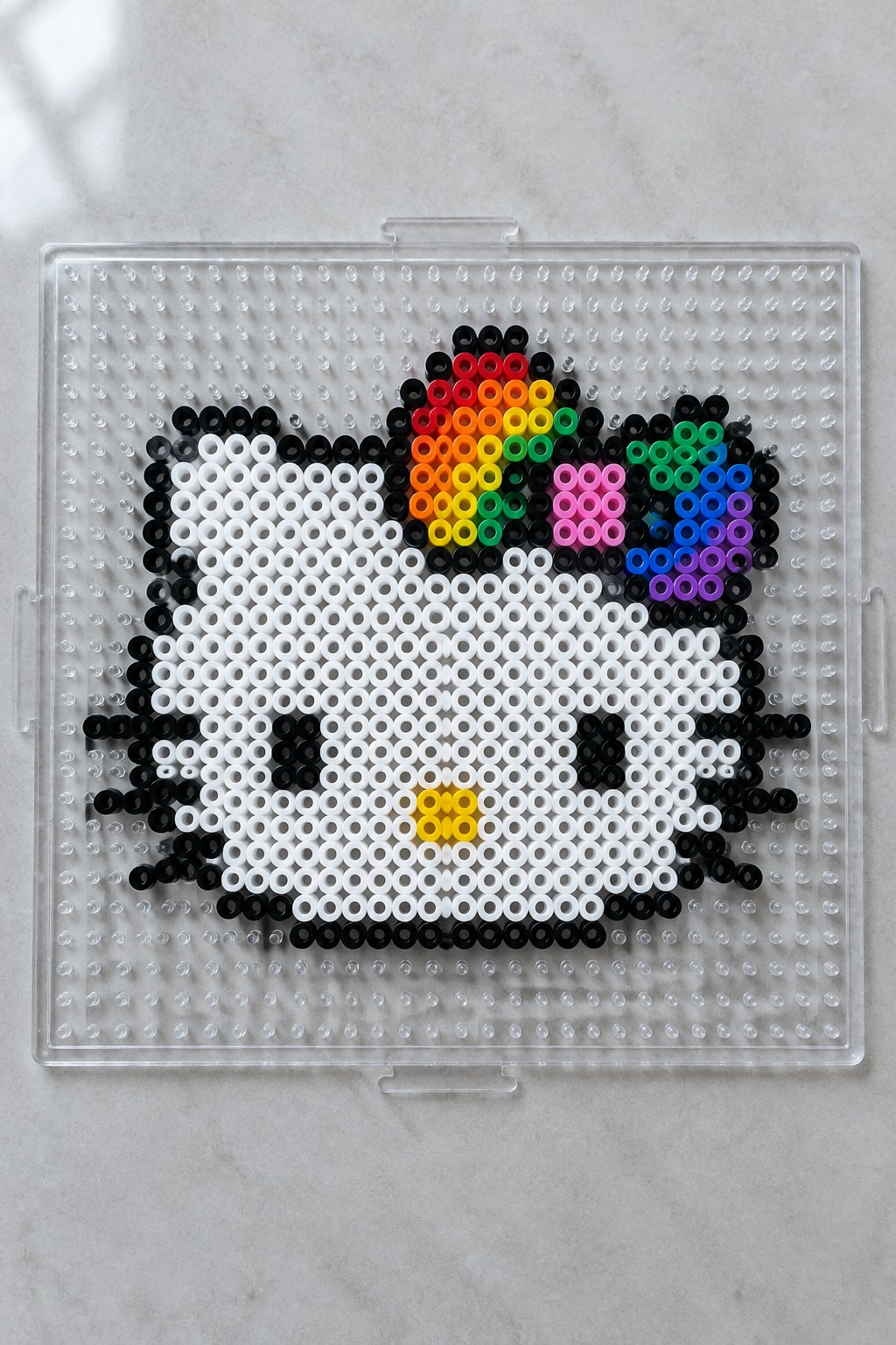 Perler bead cat face with rainbow accents on clear pegboard tray