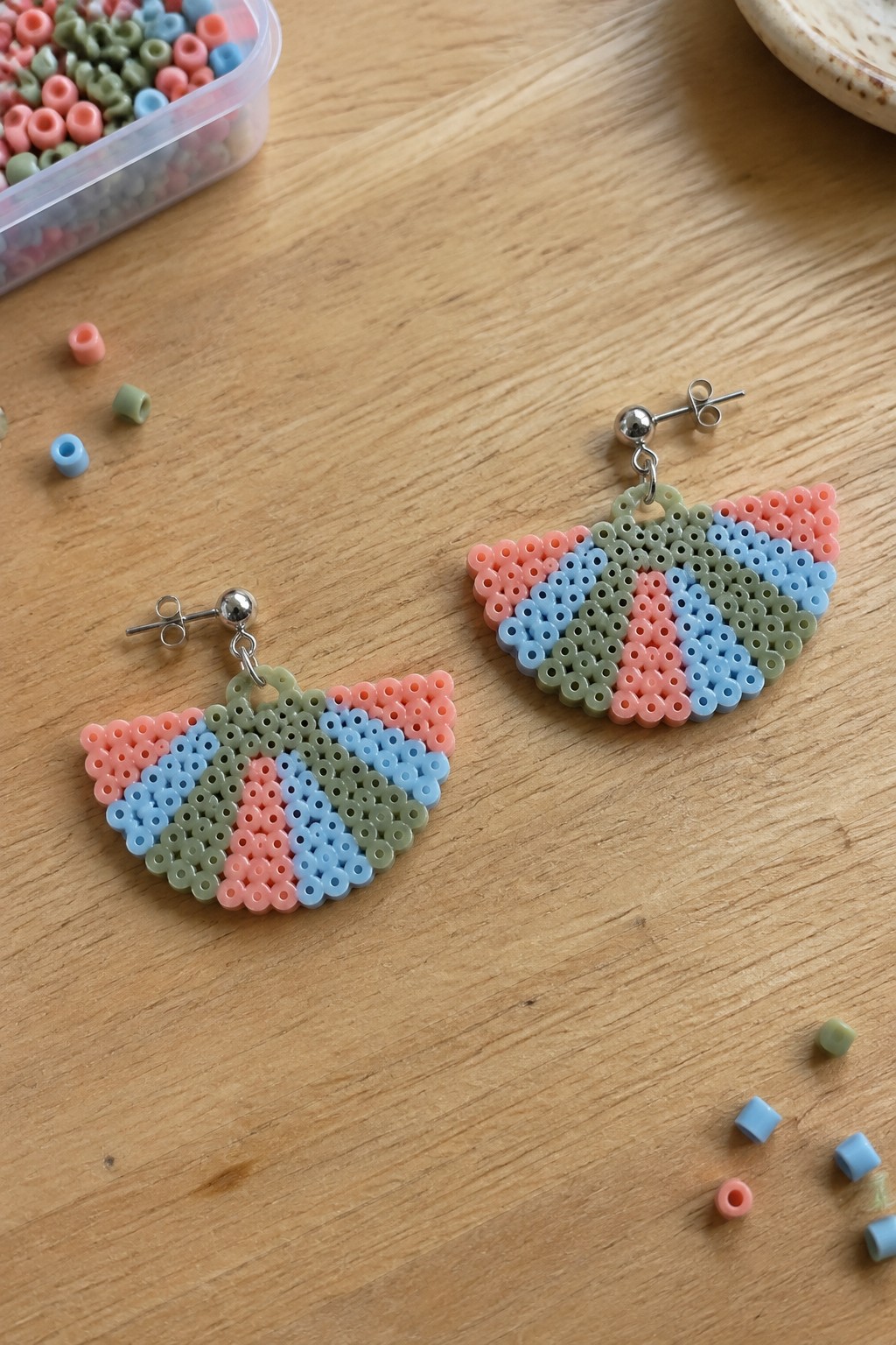 Pair of colorful perler bead fan earrings on wooden table with loose beads