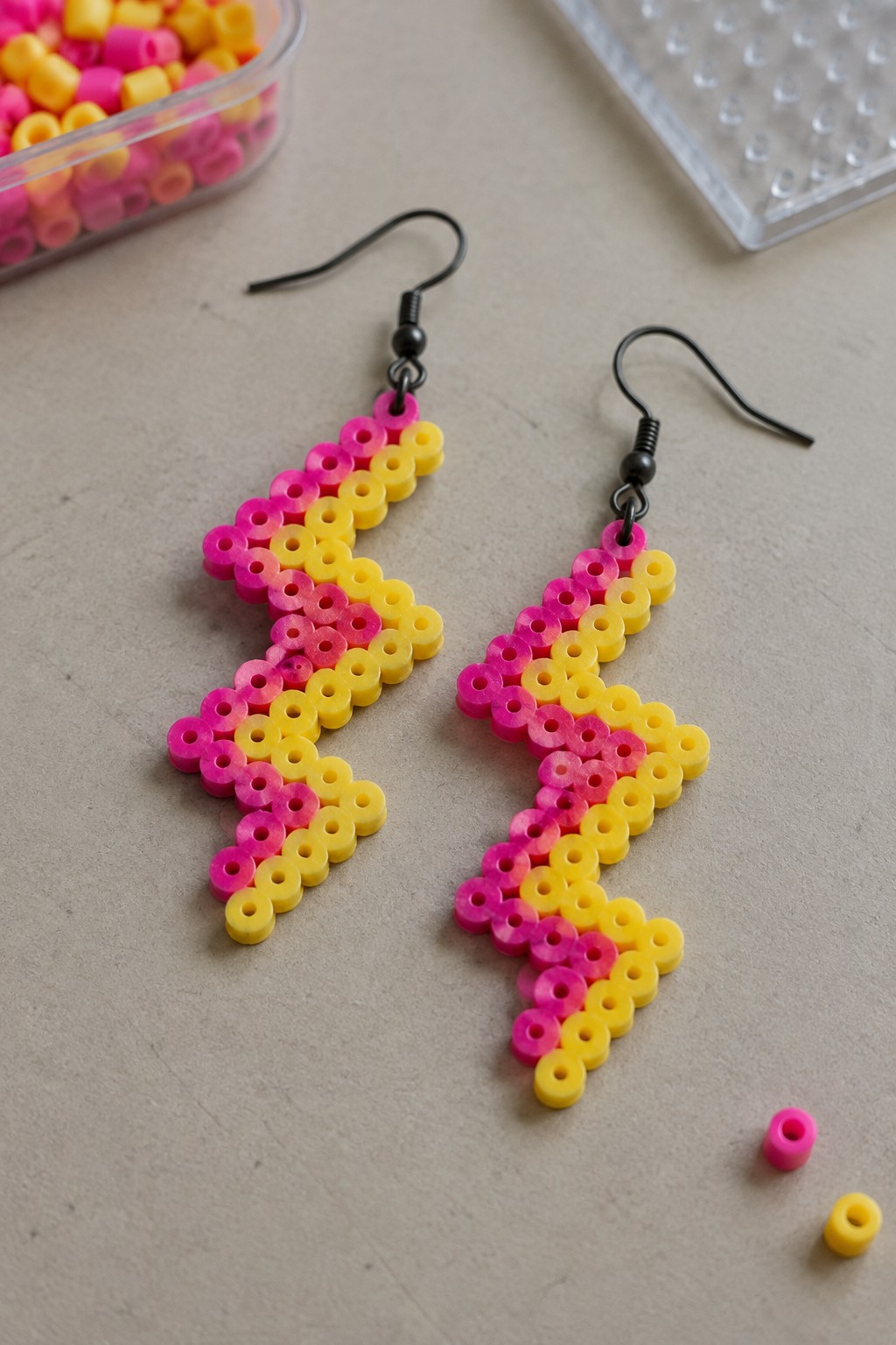 Perler bead lightning bolt earrings in pink to yellow gradient colors on black hooks.