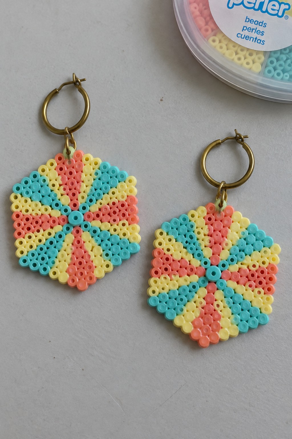Two colorful Perler bead earrings with pink, yellow, turquoise patterns on gold hoops