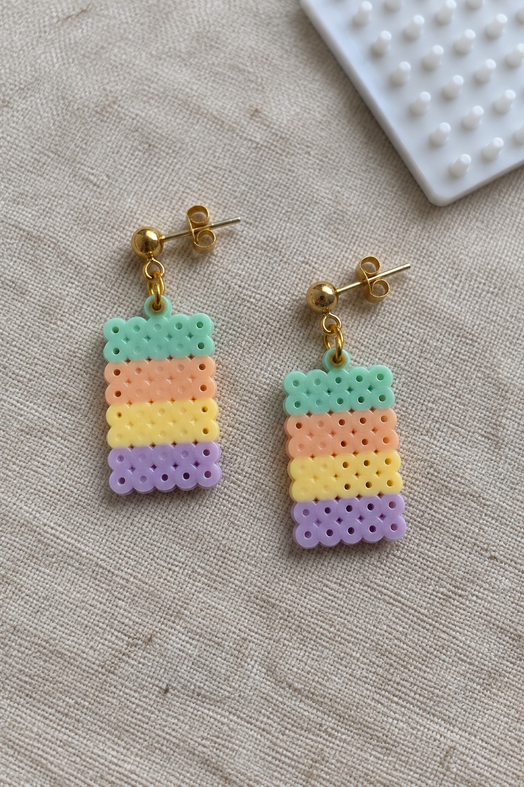 Pastel striped perler bead dangle earrings with gold posts on fabric