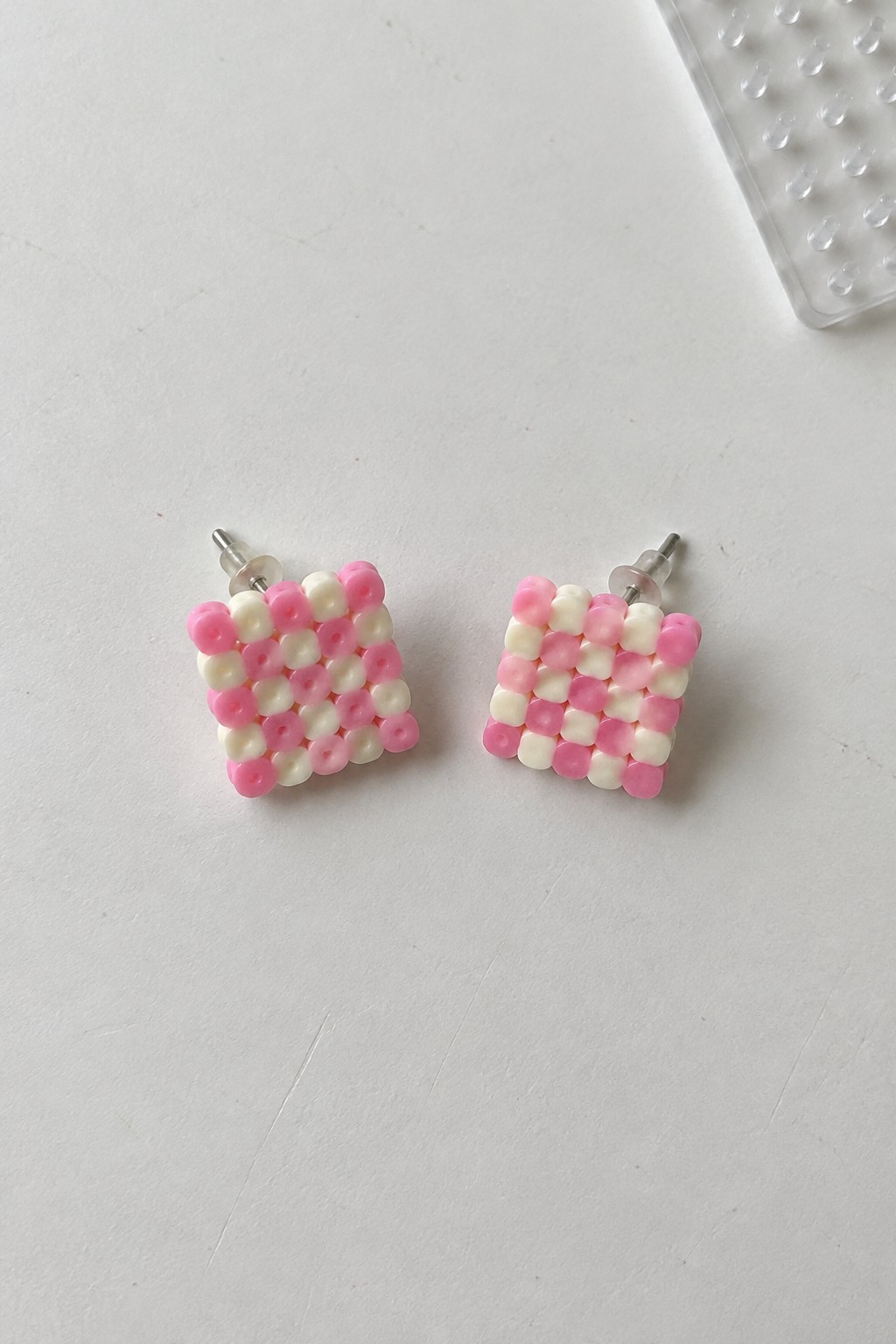 Pair of pink and white beaded square stud earrings on white surface