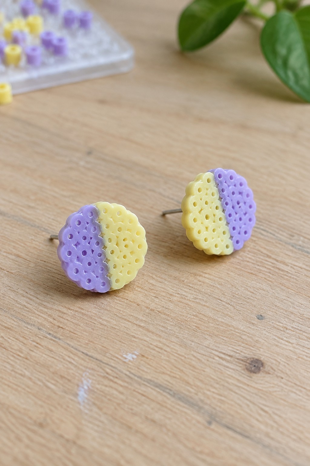 Two purple and yellow perforated round earrings on light wood with beads.