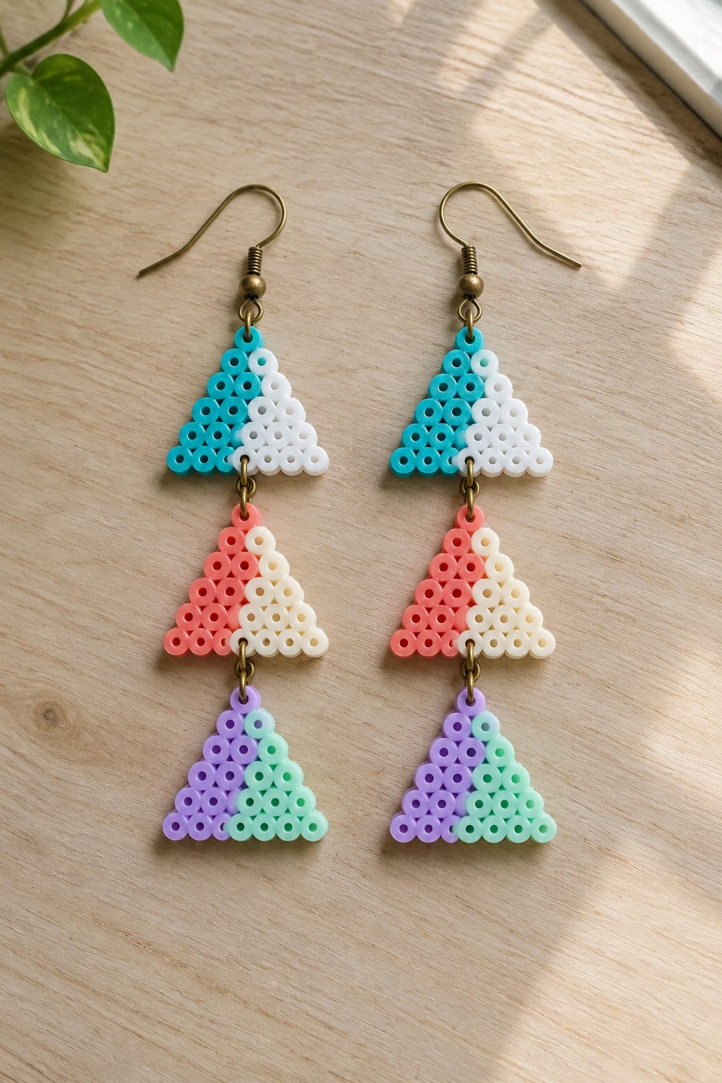 Pair of colorful perler bead triangle dangle earrings on wooden surface