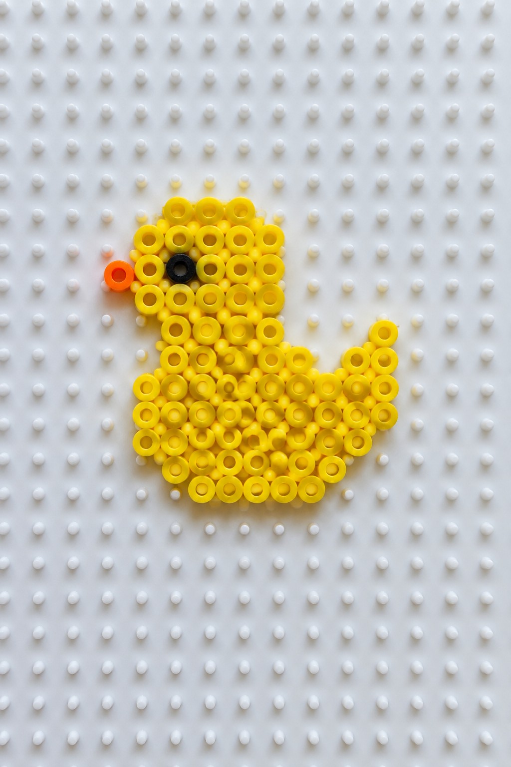 Yellow perler bead duck with orange beak and black eye on pegboard