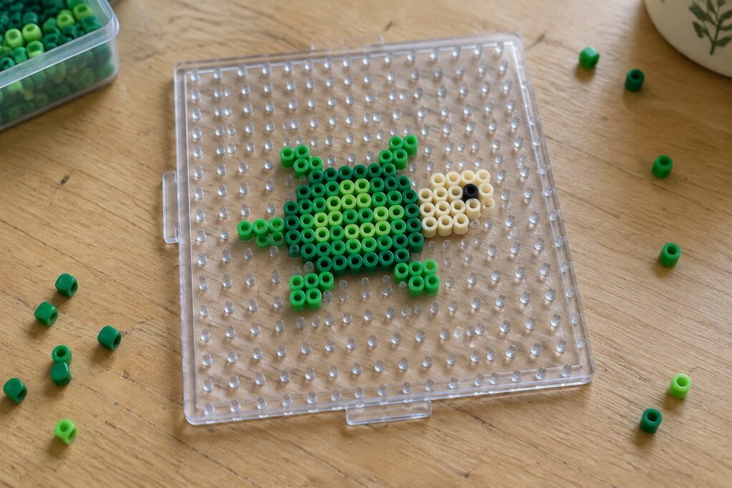 17 Small Perler Bead Patterns Using Fewer Beads Green Perler beads forming a sea turtle on clear pegboard with loose beads scattered nearby