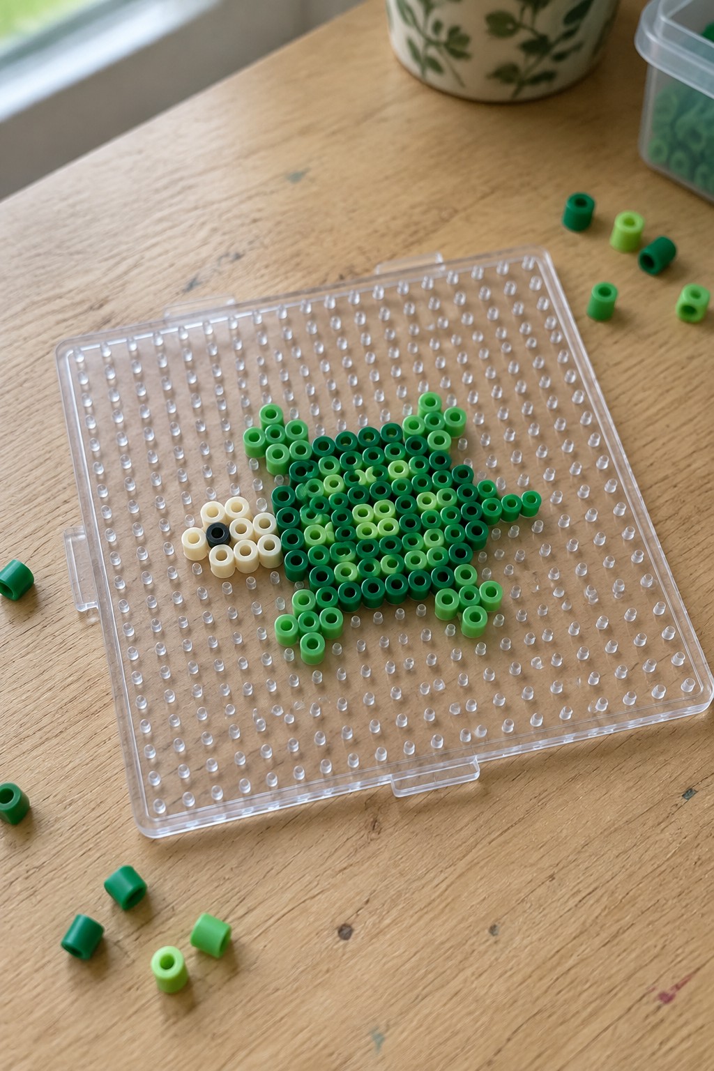 Green Perler beads forming a sea turtle on clear pegboard with loose beads scattered nearby