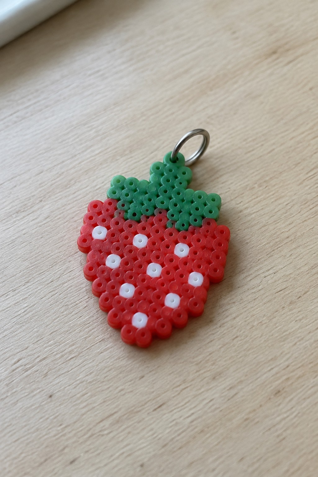 Red perler bead strawberry keychain with green leaves and silver ring on wood
