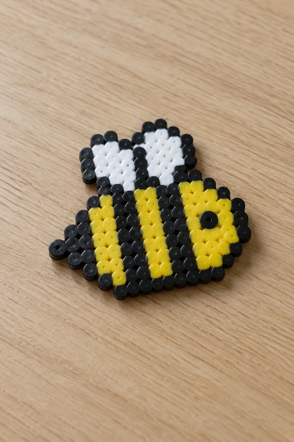 Black and yellow perler bead bee with white wings on wood
