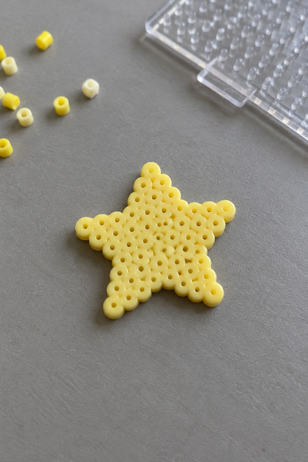 Yellow Perler bead star on gray surface with loose beads and clear pegboard