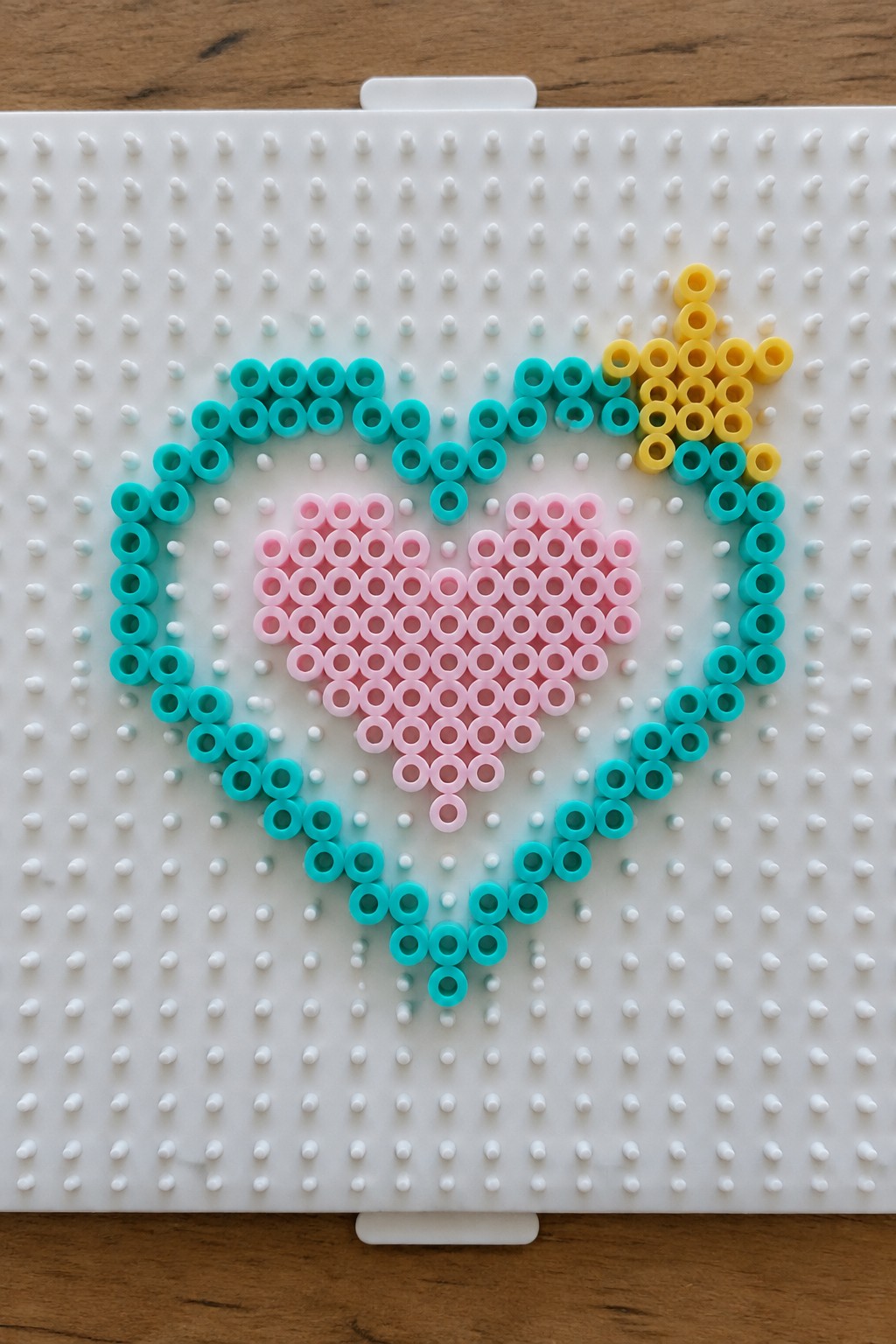 Turquoise heart outline with pink center and yellow arrow of perler beads