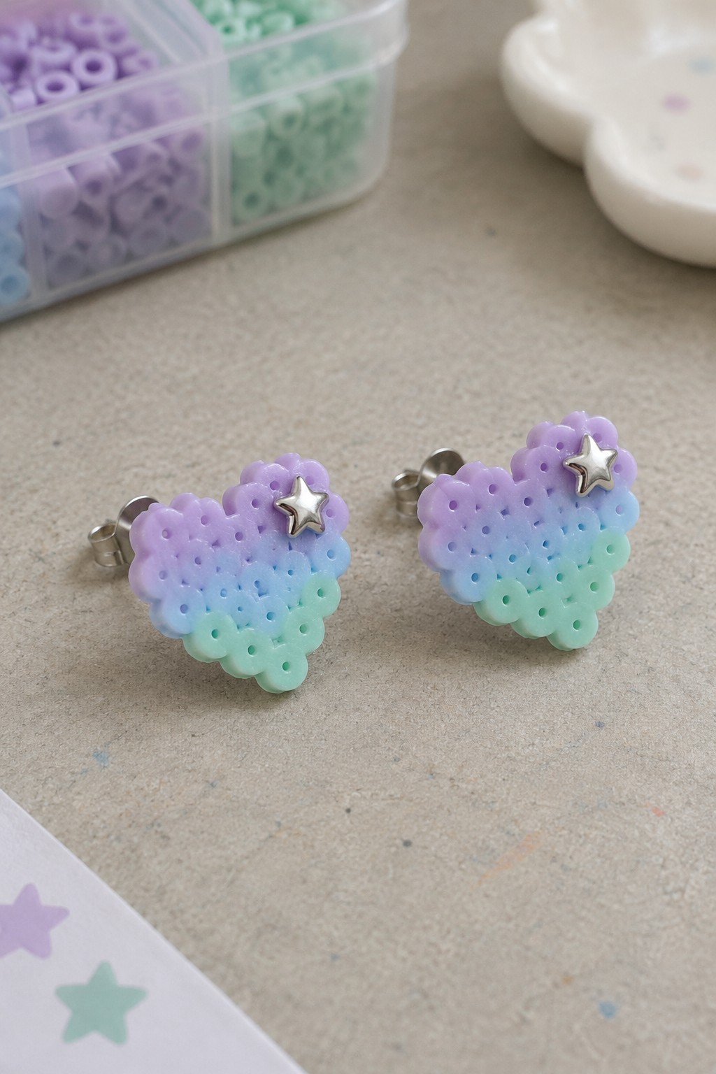 Two pastel gradient heart beaded earrings with silver stars beside bead organizer