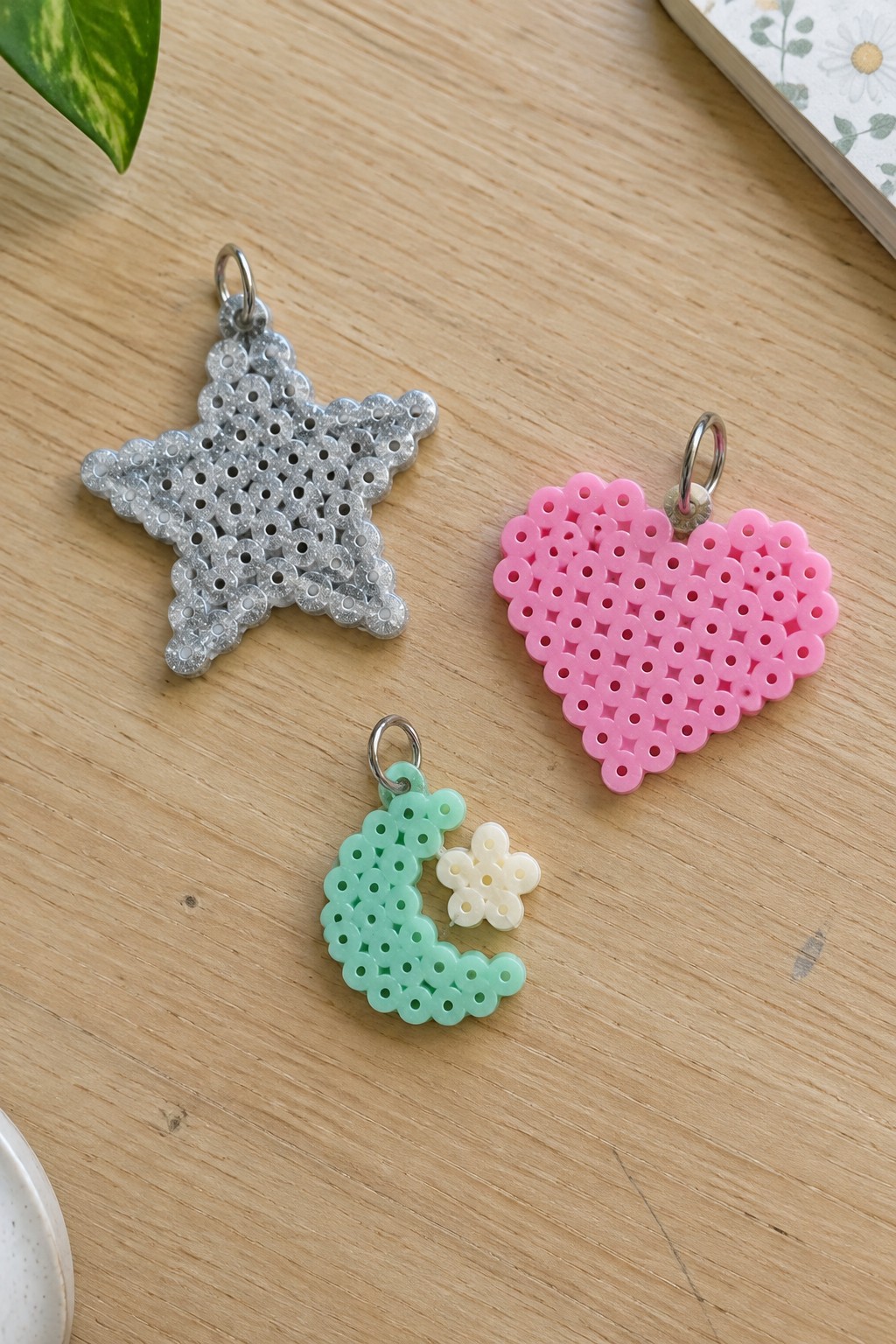 Glittery silver star, pink heart, and mint moon flower perler bead charms on wood