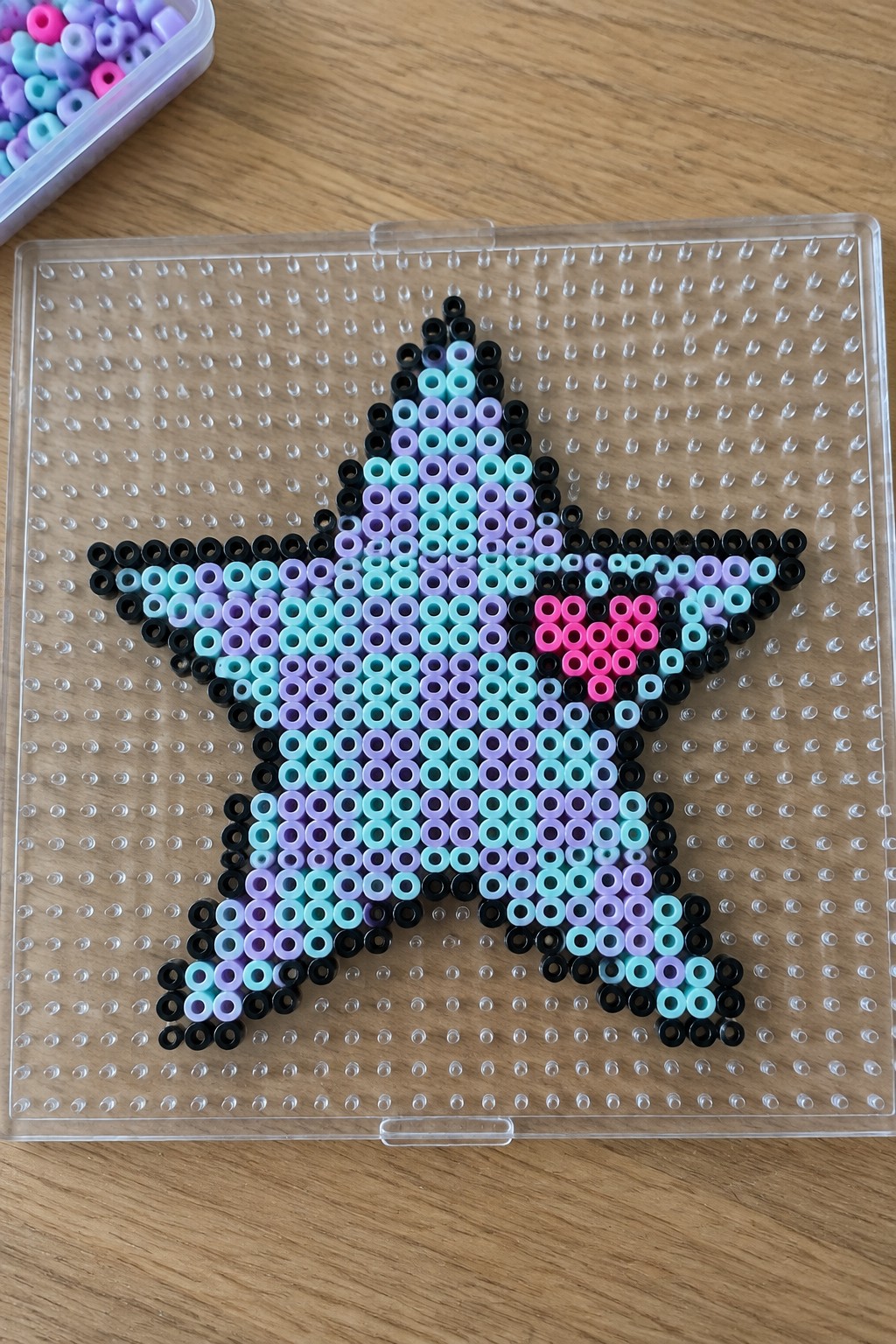Colorful perler bead star with black outline and pink heart on pegboard