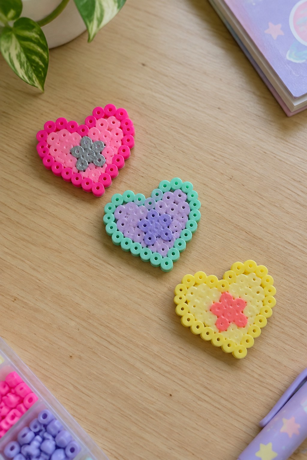 Three colorful perler bead hearts with flower centers on a wooden table