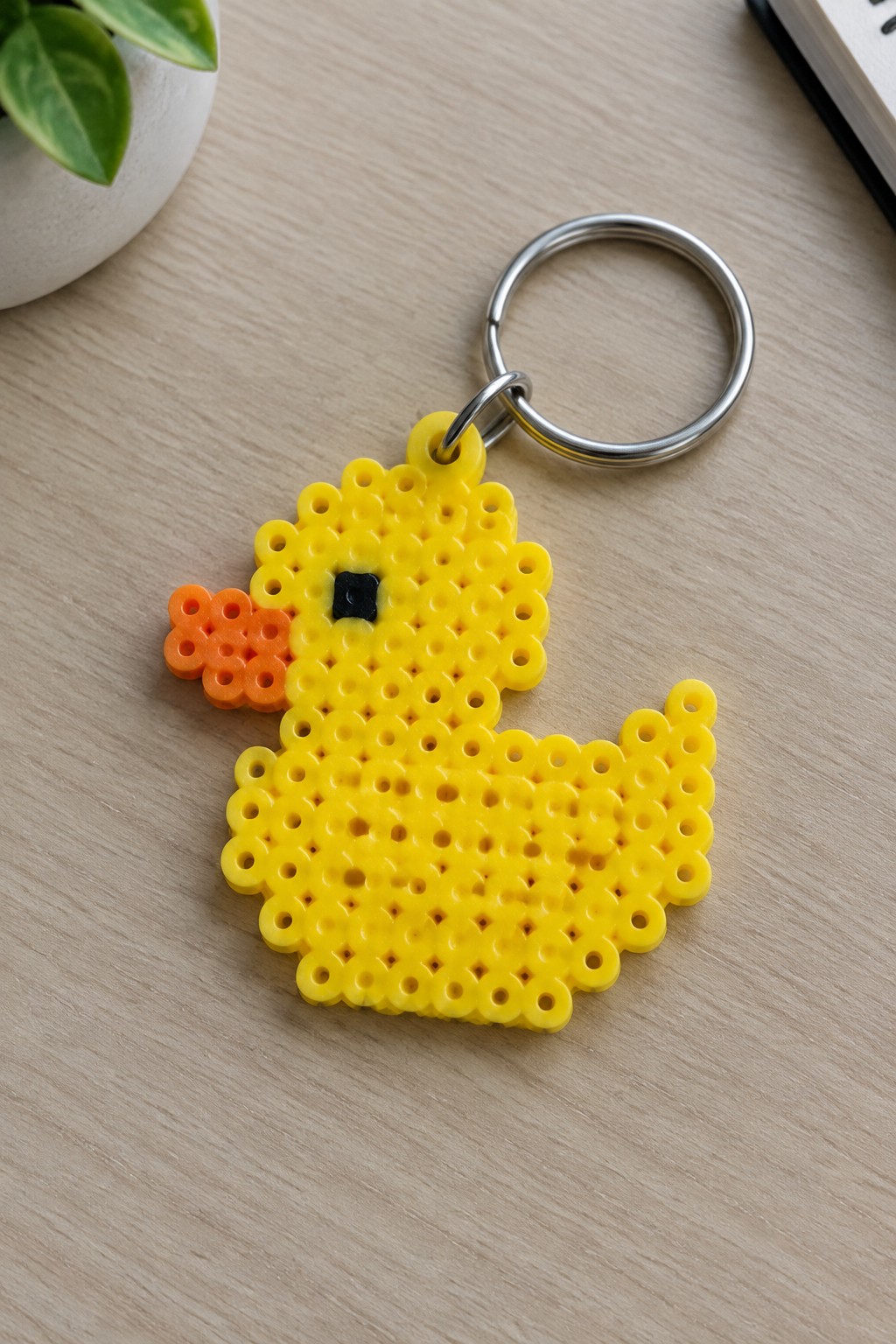 Yellow perler bead duck keychain with orange beak, black eye, metal ring on wood