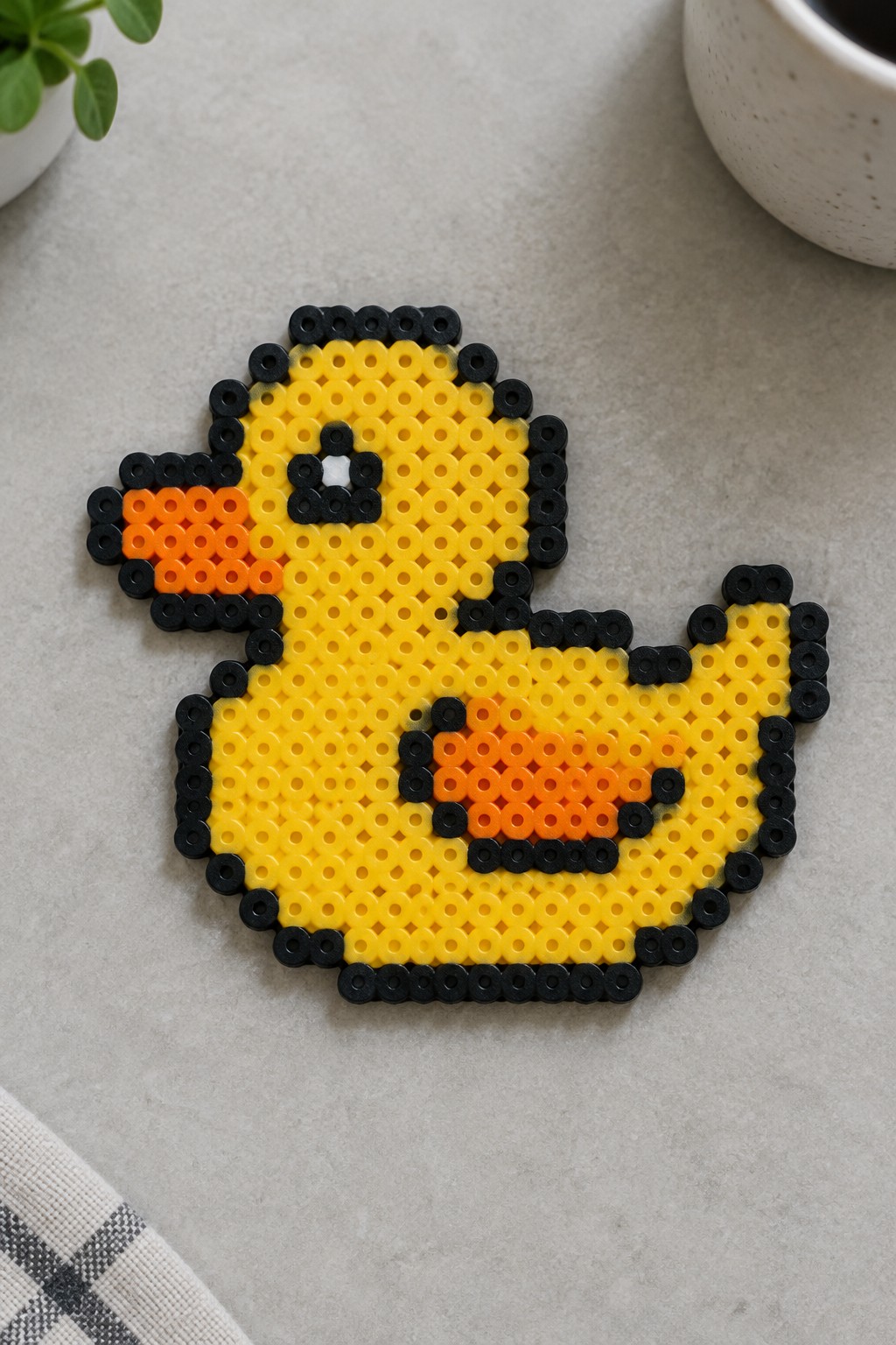 Yellow perler bead duck with black outline, orange beak and wing on gray surface.