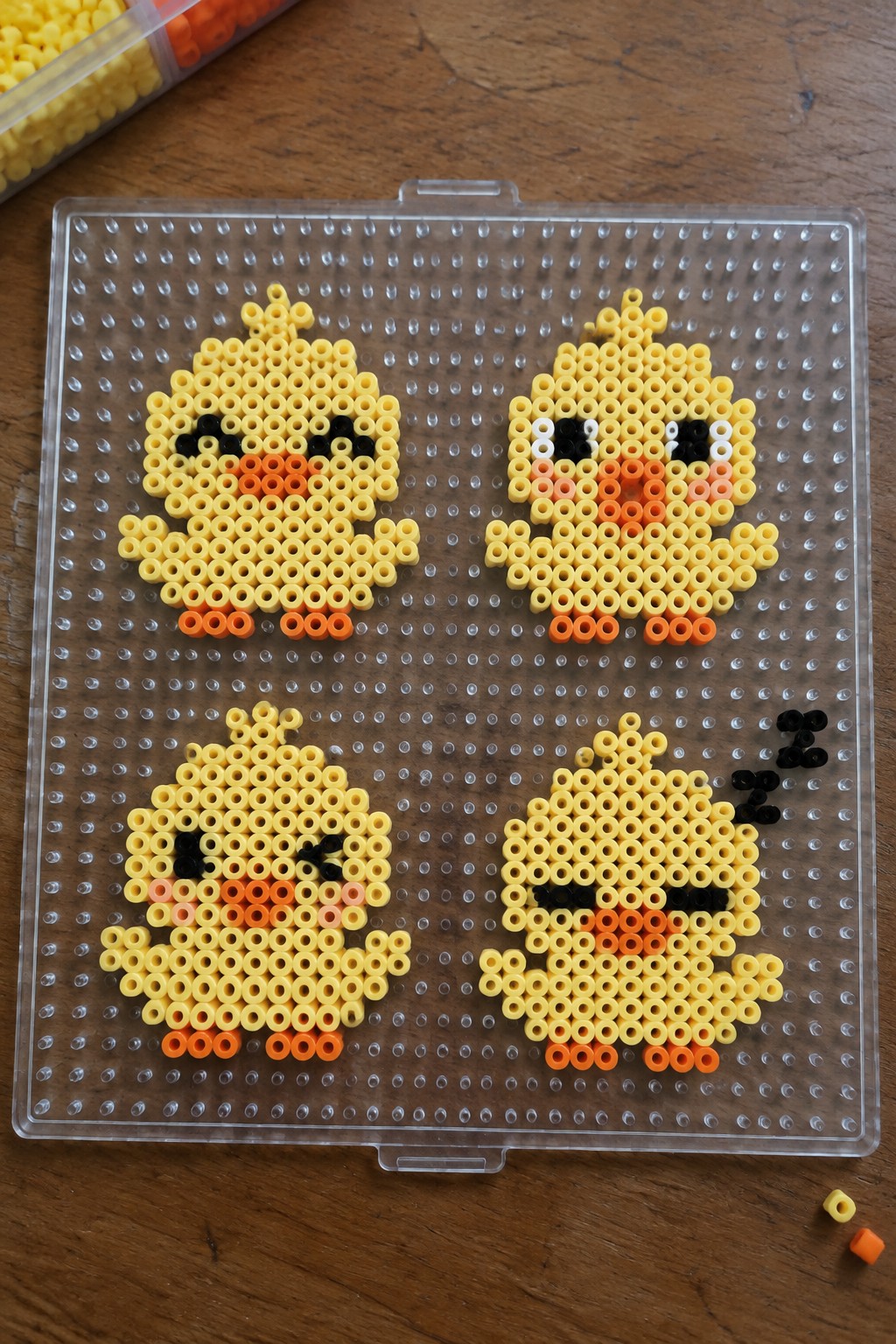 Four yellow perler bead chicks on a clear pegboard over wood.