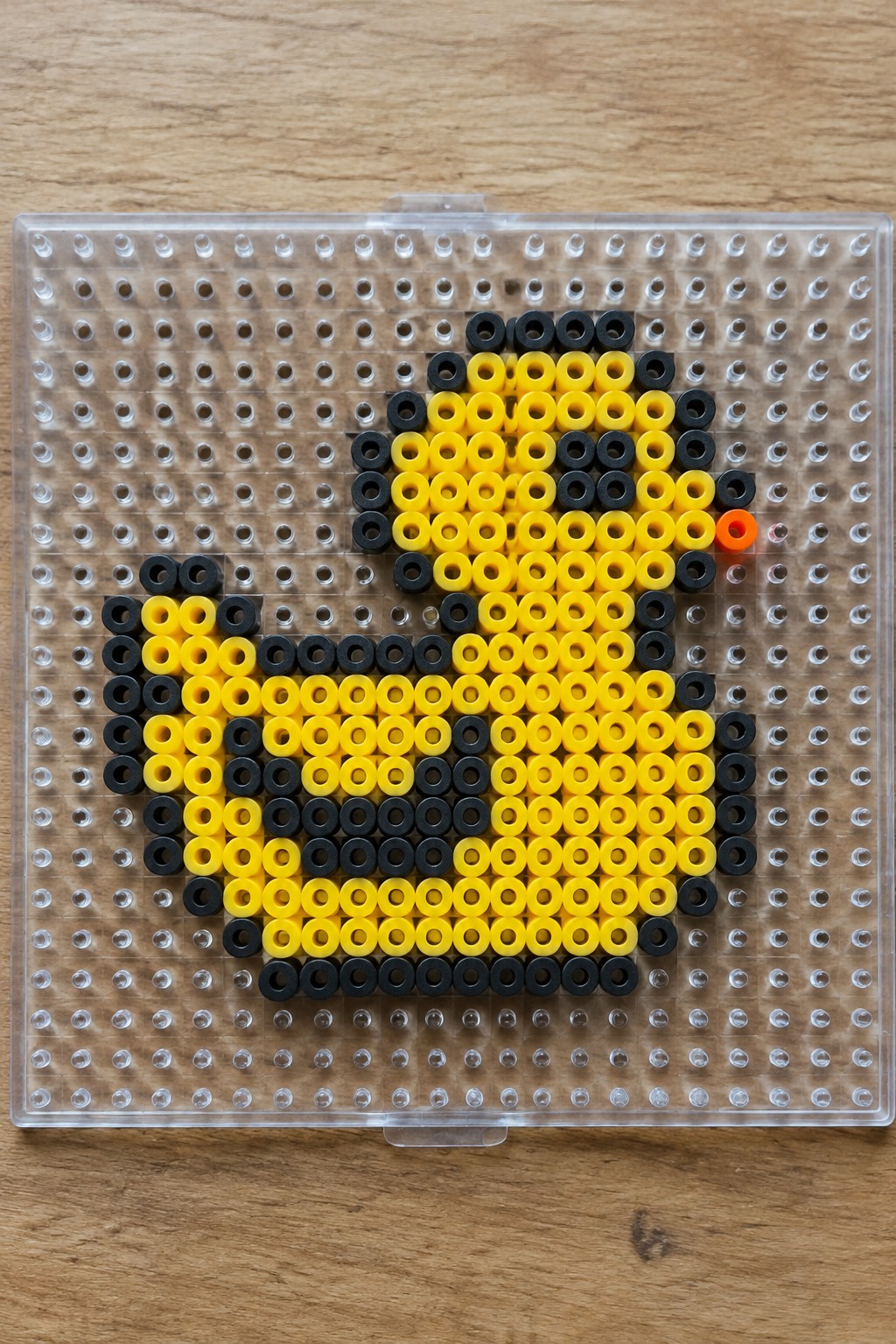 Yellow duck perler bead pixel art with black outline and orange beak on pegboard