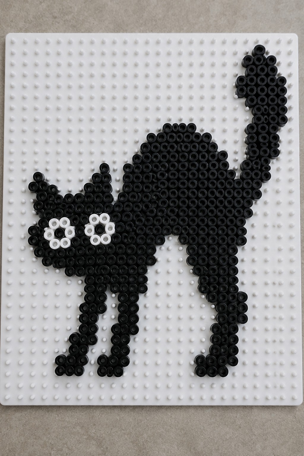 Black perler bead cat with white eyes on pegboard