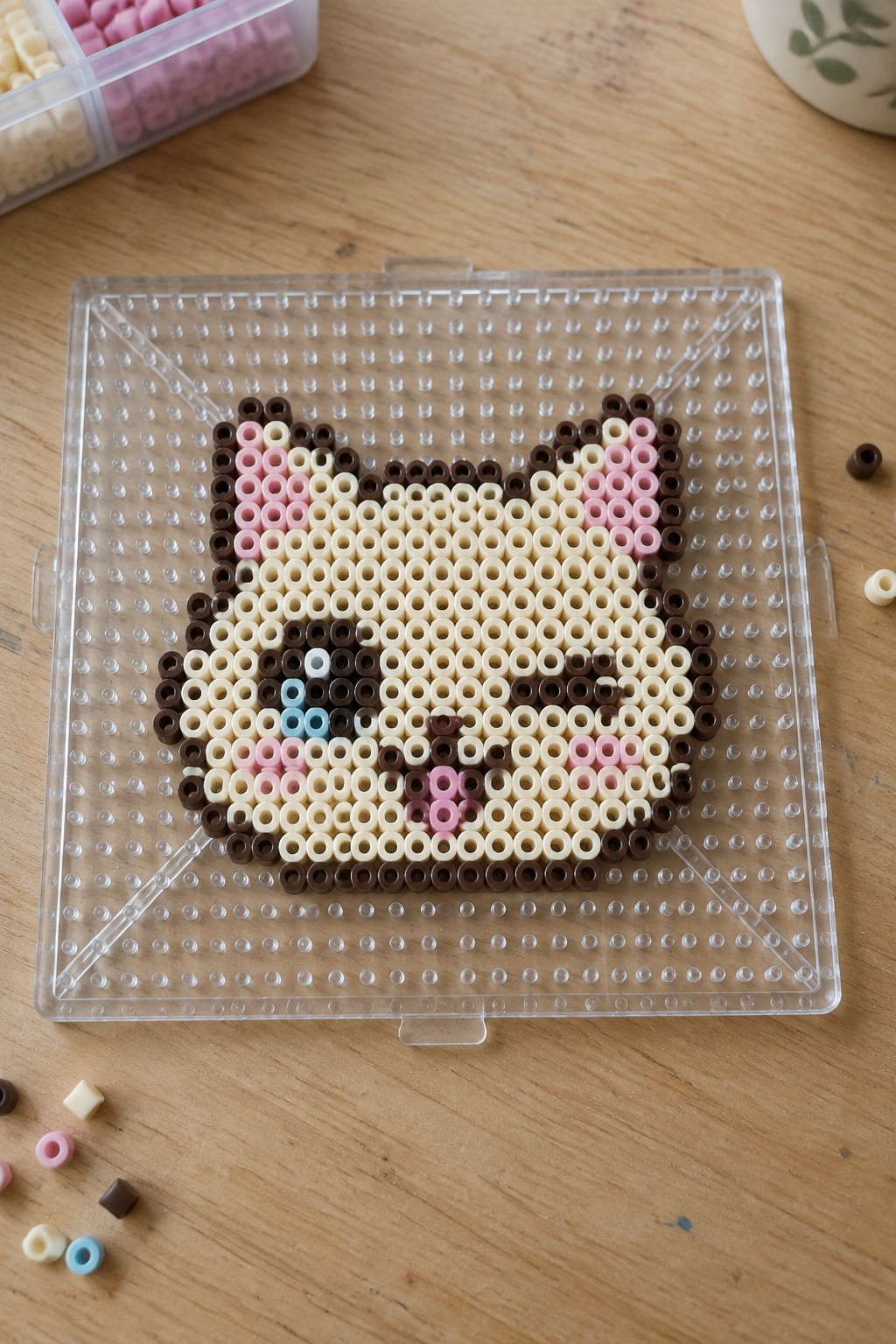 Cat face pixel art made with perler beads on clear pegboard