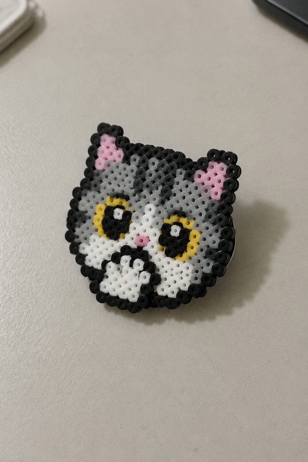 Perler bead cat face with pink ears, yellow accents, and black outlines.
