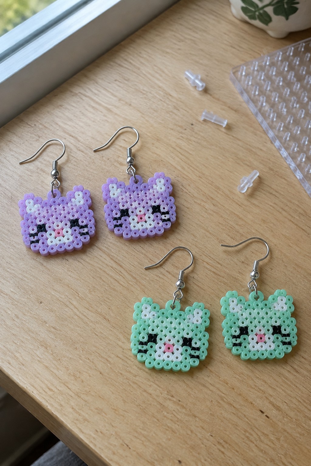 Four perler bead cat earrings in purple and mint green on wood table