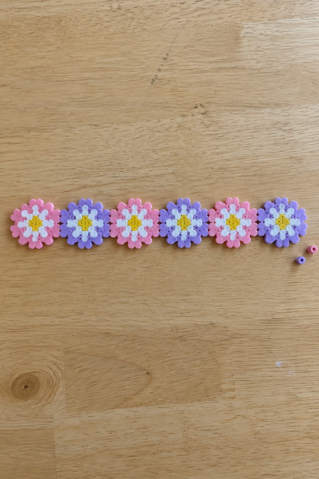 Six pink and purple flower perler beads lined up on wooden table