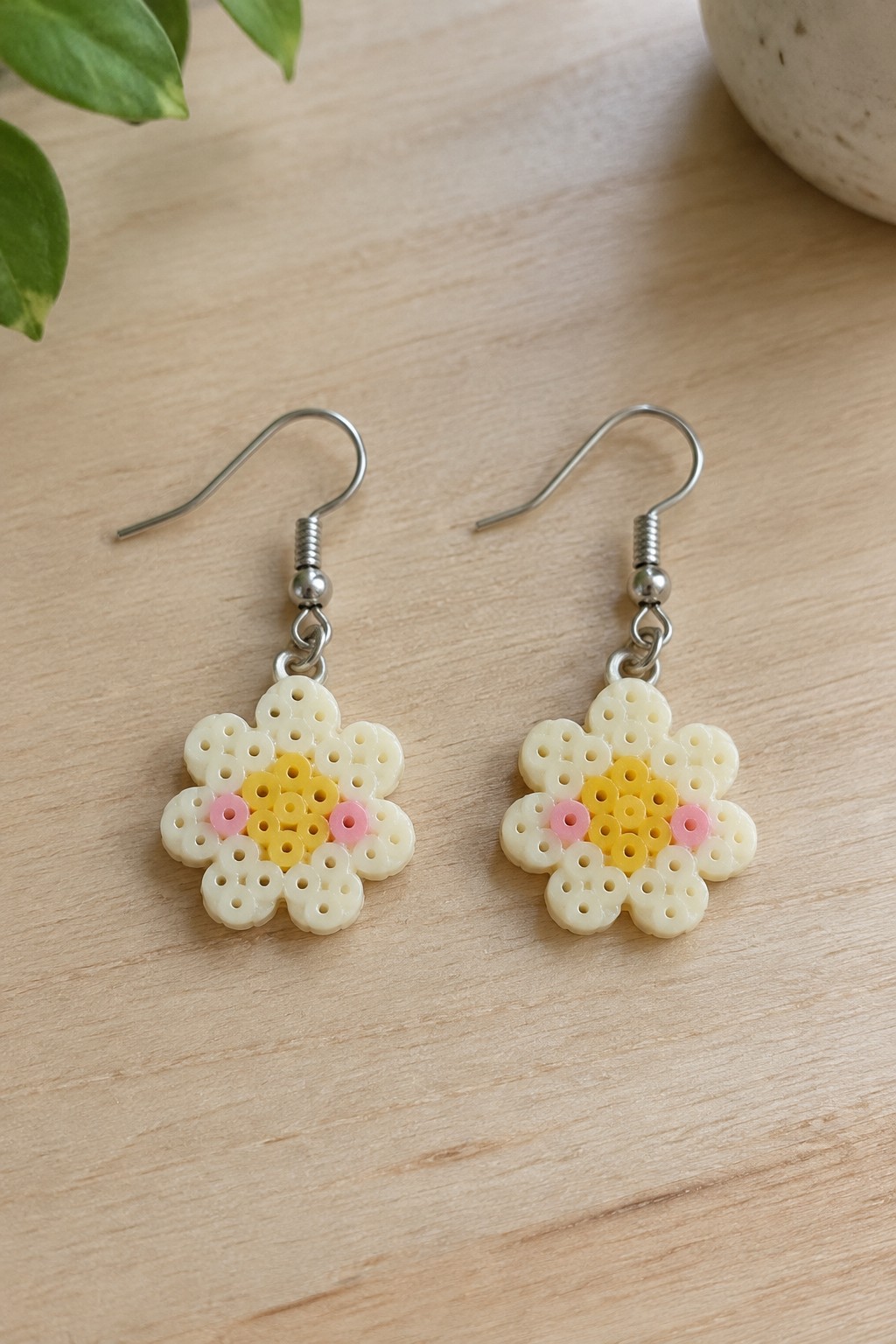 Pair of white perler bead flower earrings with yellow centers and pink accents on wood