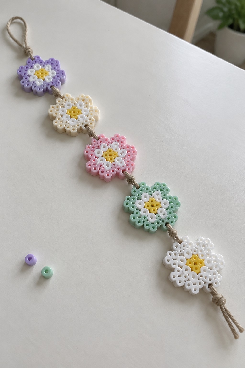 Five daisy Perler bead flowers with yellow centers, white rings, and colored borders strung on twine.