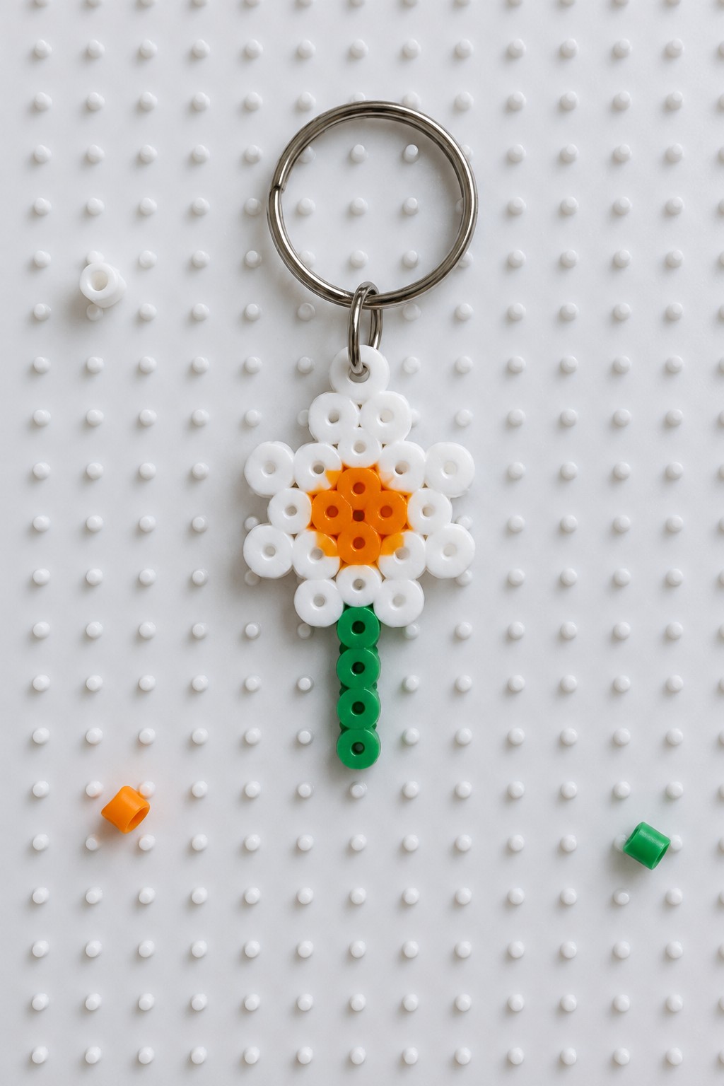 Perler bead flower keychain with white petals, orange center, green stem on metal ring