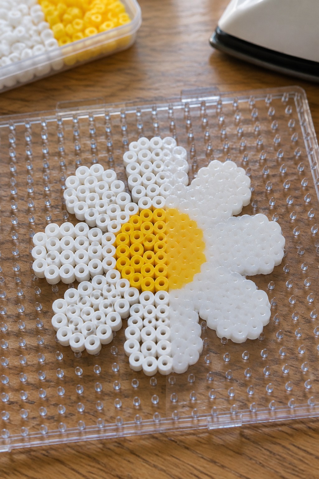 Perler bead daisy with white petals and yellow center on clear pegboard.