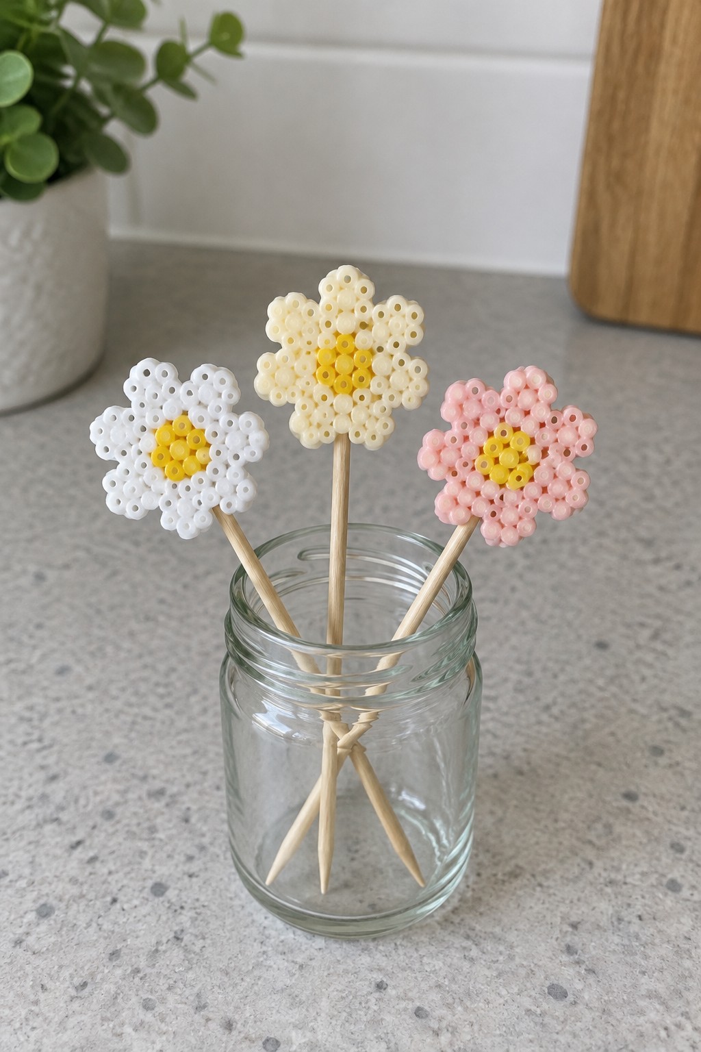 Three perler bead flowers in white, pink, and yellow on sticks in a jar