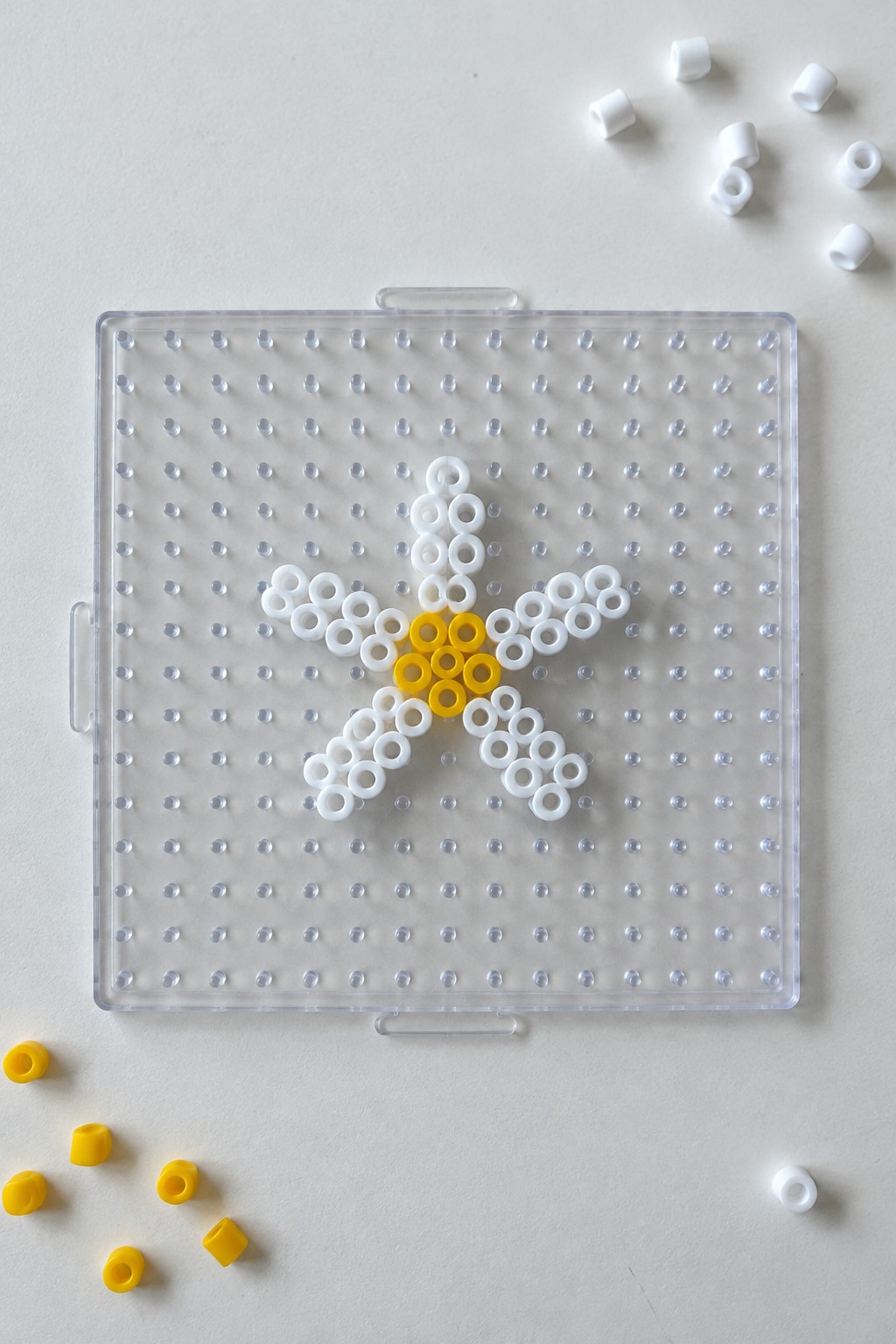White and yellow beaded star on transparent pegboard with loose beads nearby