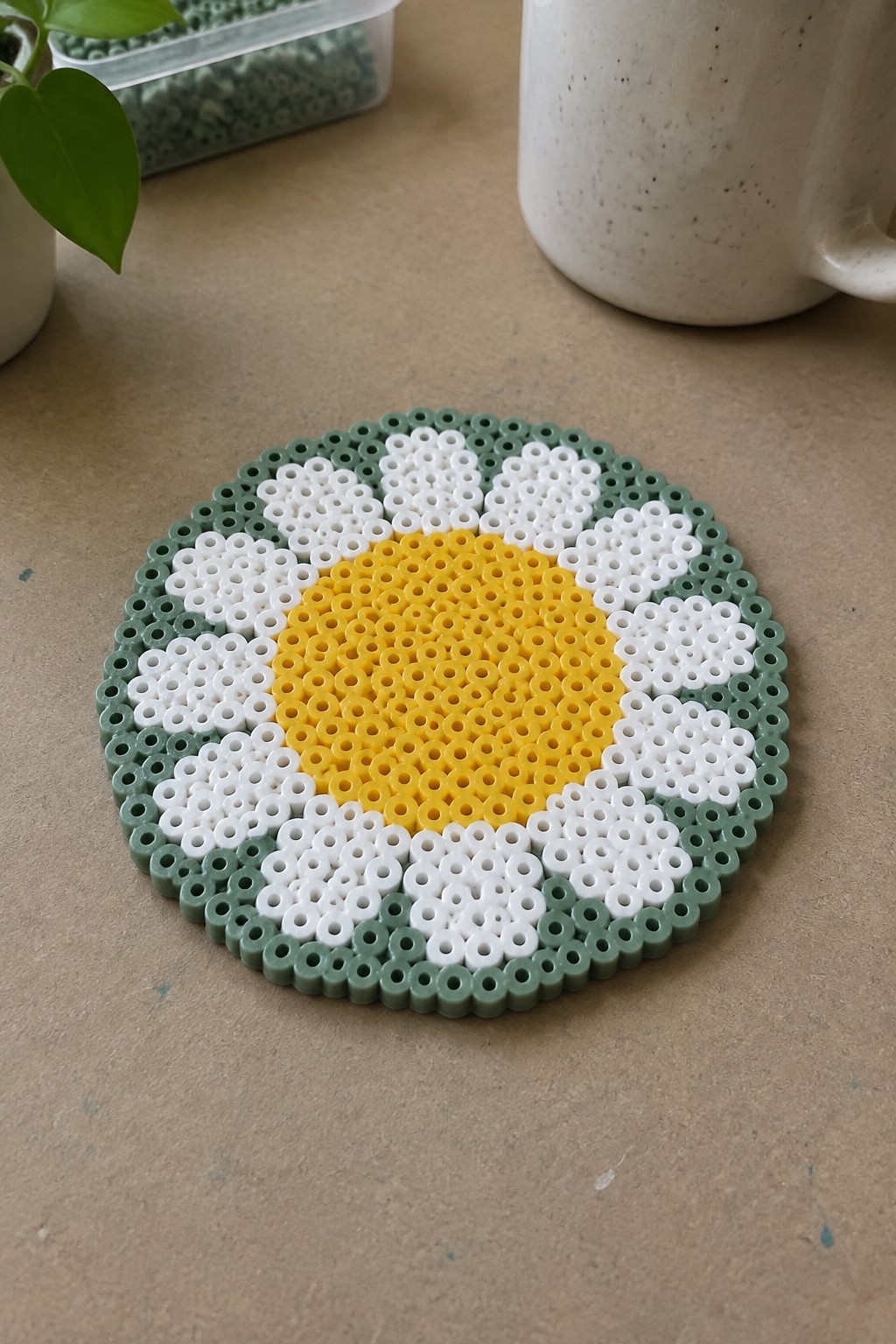 Circular perler bead daisy with yellow center, white petals, and green border.