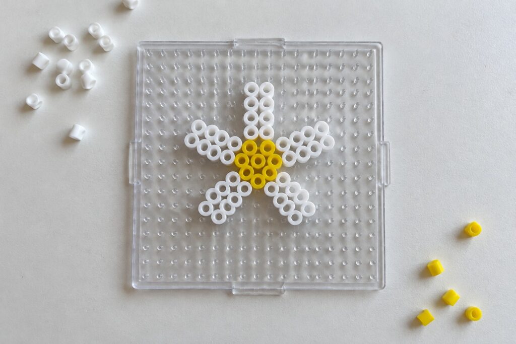 White and yellow beaded star on transparent pegboard with loose beads nearby