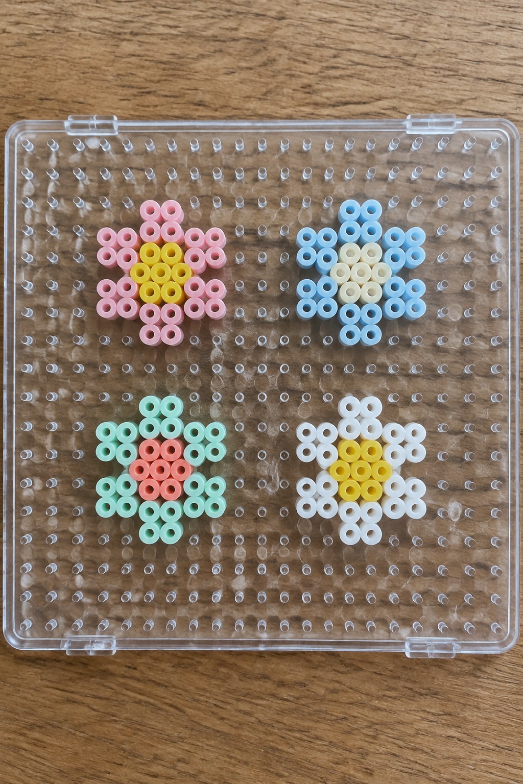 Four colorful beaded flowers on a clear plastic pegboard.
