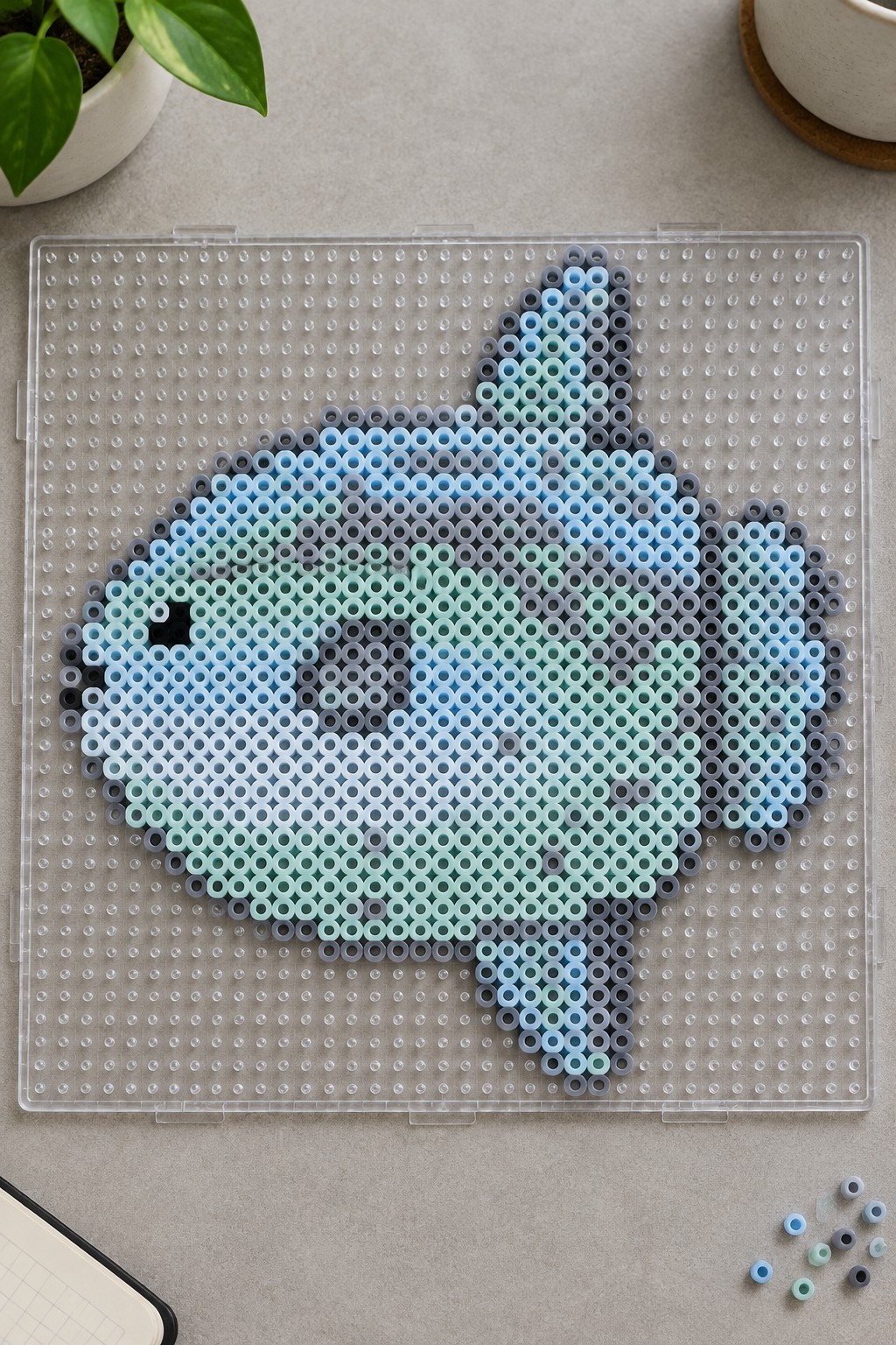 Perler bead fish in blue, teal, and gray shades on a clear pegboard.