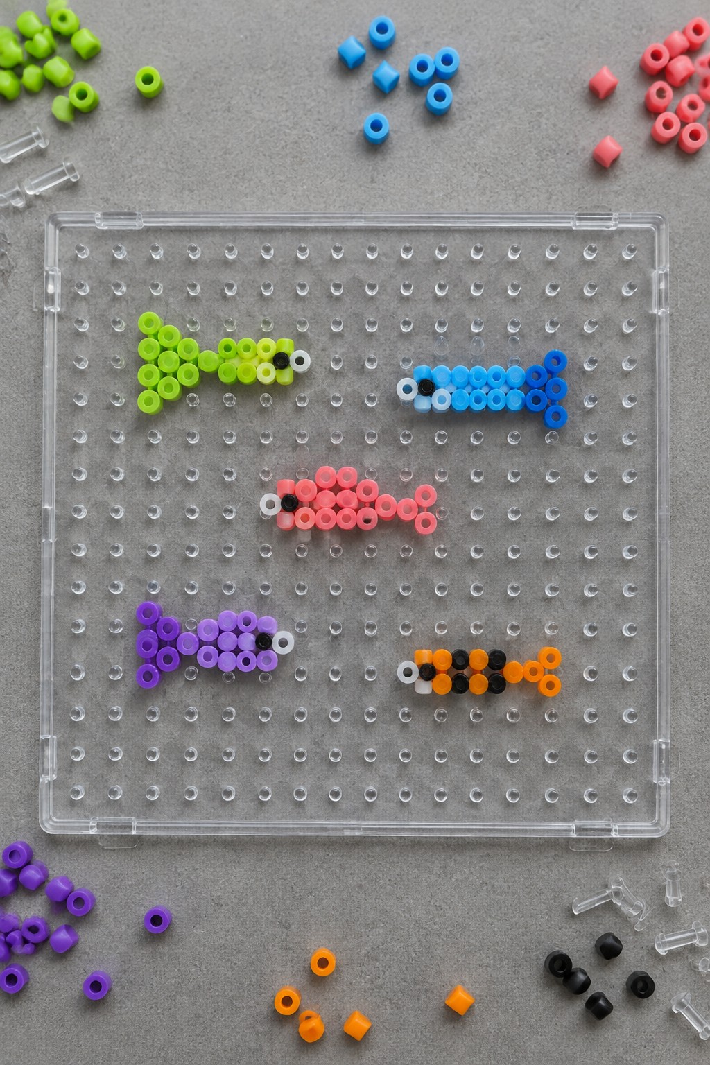 Colorful beaded fish on clear pegboard surrounded by scattered loose beads.