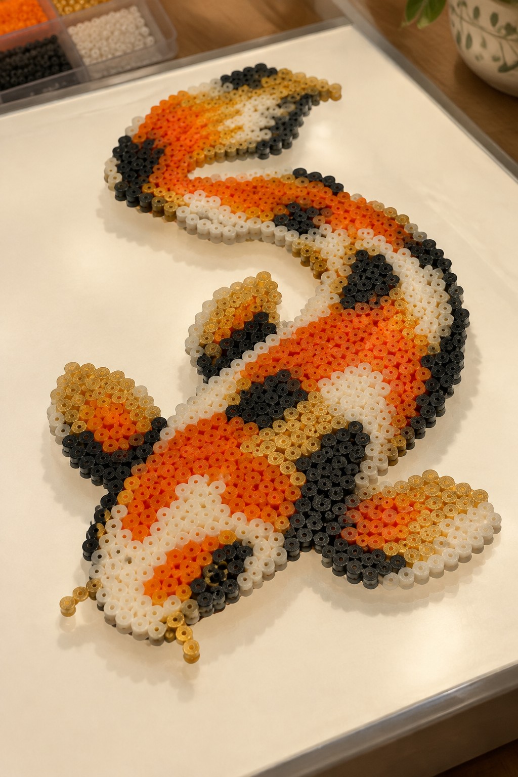 Perler bead koi fish in orange, black, and white on white tray.