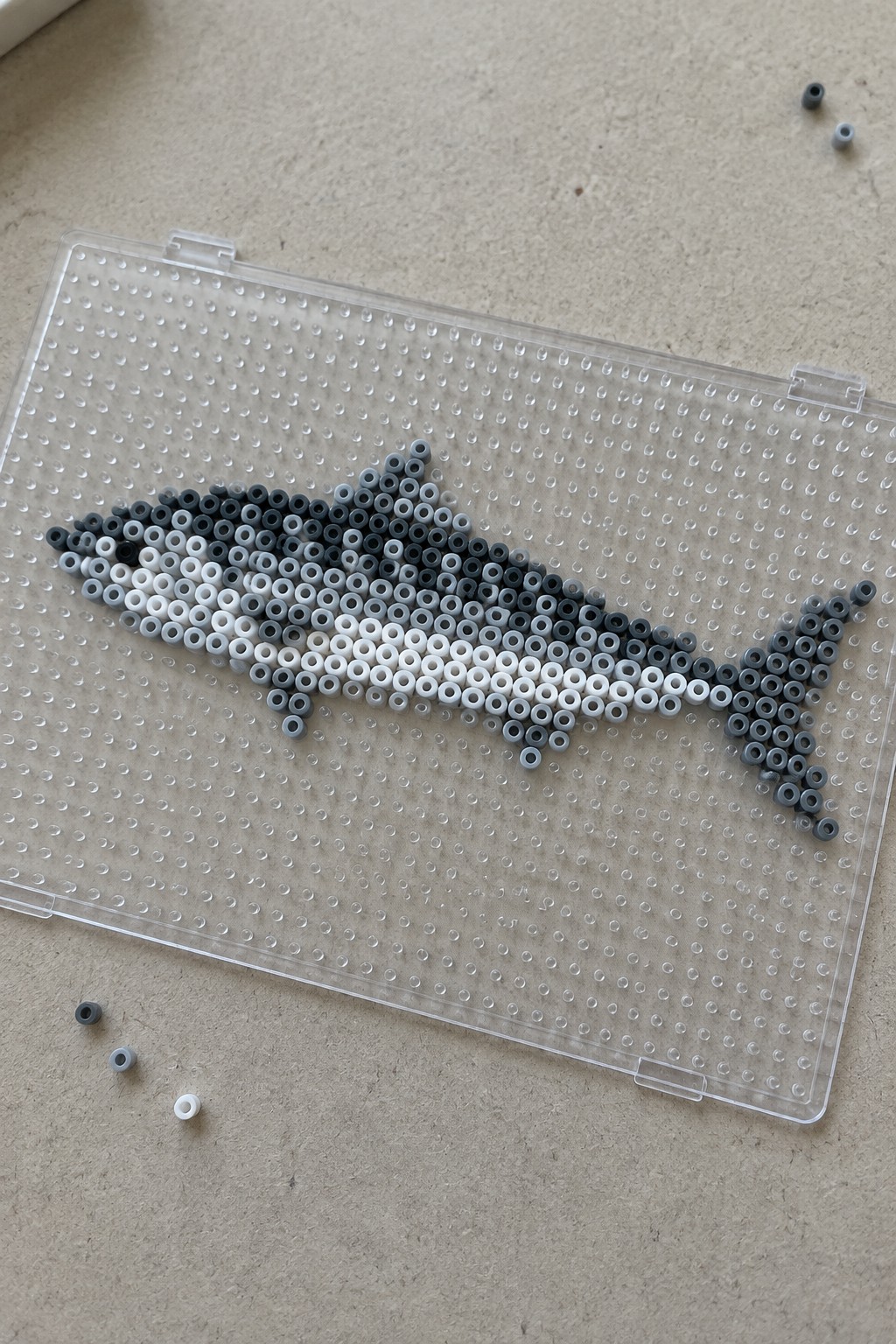 Beaded shark in black, white and gray on clear pegboard with loose beads