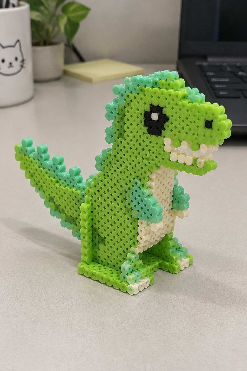Green perler bead T-Rex dinosaur with black eye on desk
